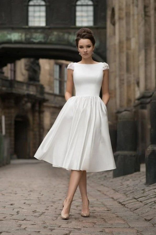 a woman in a white dress is standing on a brick road and posing for the camera