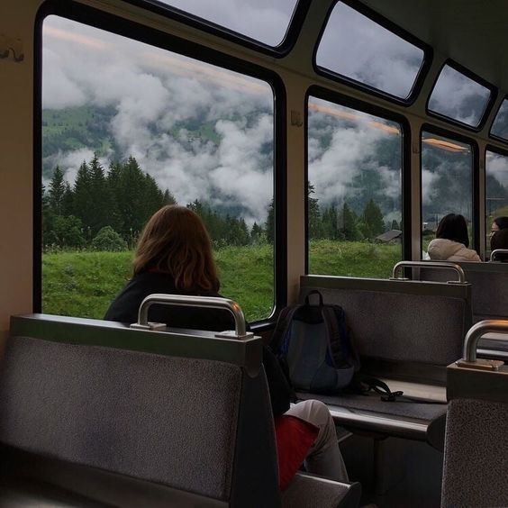 people are riding on a train with mountains in the background and clouds coming out of the window