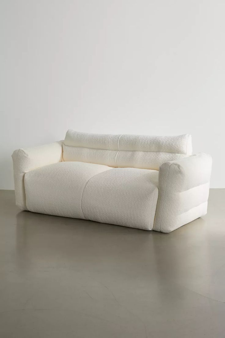 a white couch sitting on top of a cement floor next to a wall and window