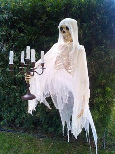 a skeleton hanging from a wall with candles in it's hands and wearing a ghost costume