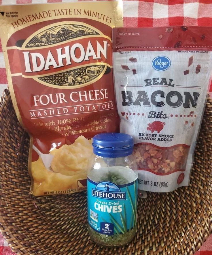 some food is sitting in a basket on a checkered tablecloth and next to two bags of chips