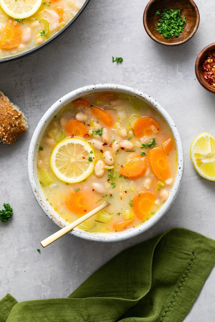 a bowl of soup with lemons, carrots and parsley on the side