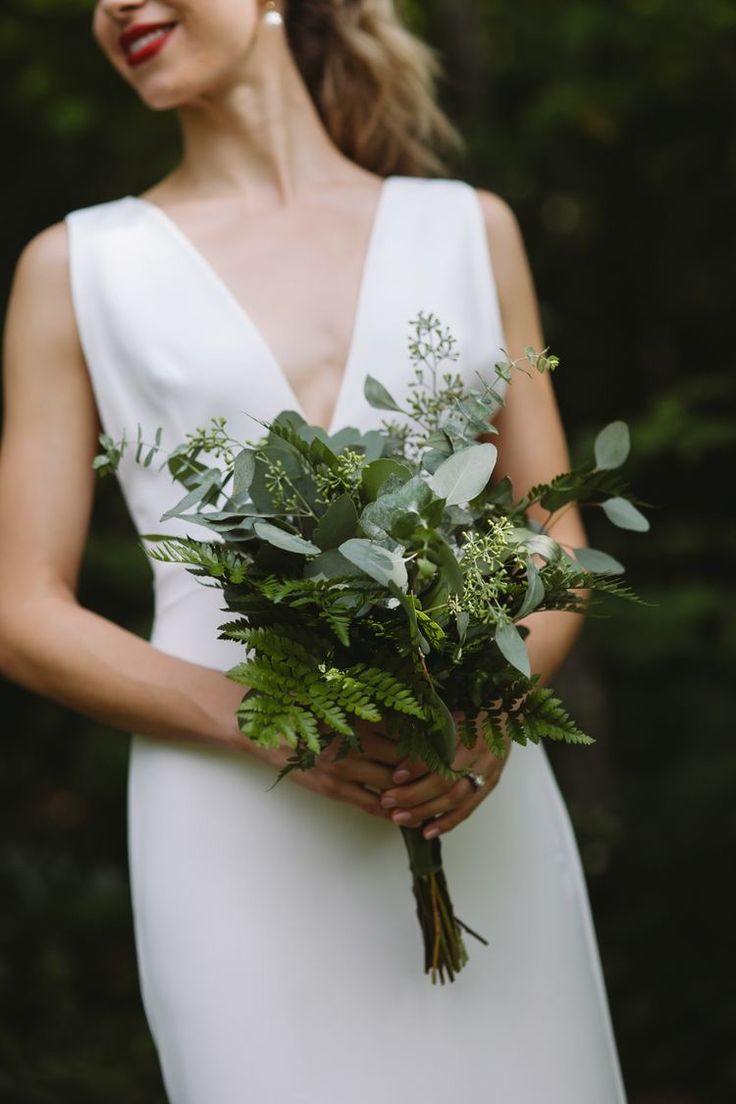 a woman in a white dress holding a bouquet of greenery