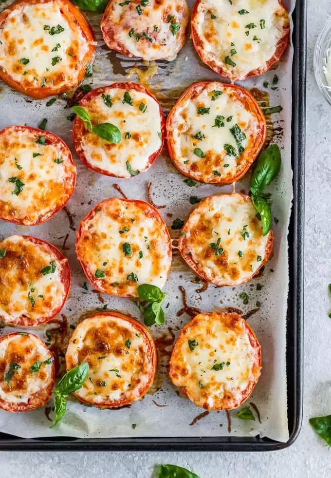 an overhead view of baked stuffed tomatoes on a baking sheet with basil leaves and cheese