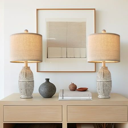 two lamps are on top of a dresser in front of a painting and vases