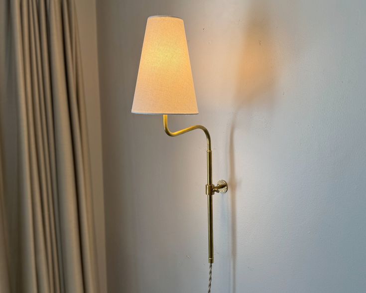 a wall lamp with a white shade on it next to a curtained window in a hotel room