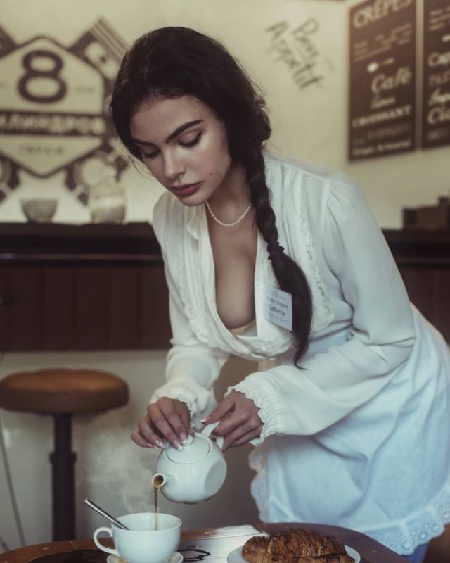 a woman pouring tea into a cup on top of a wooden table with pastries