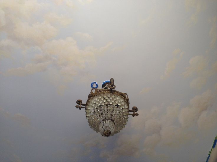 a chandelier hanging from the ceiling in a room with clouds painted on it