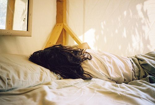 a woman laying on top of a bed under a window next to a white wall