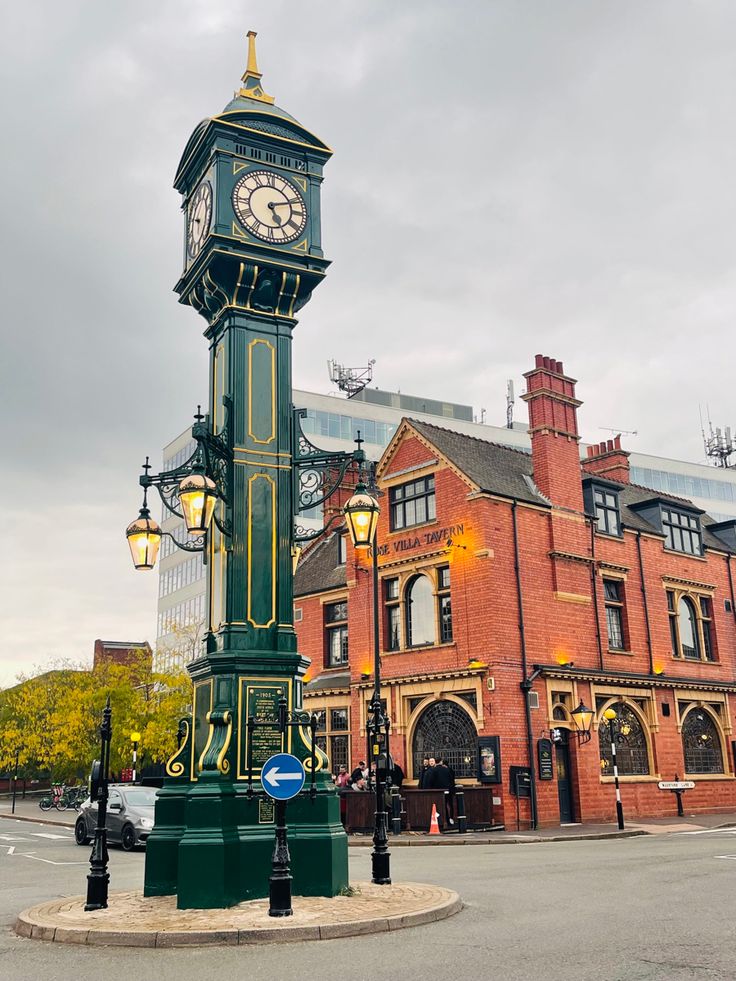 a green clock tower sitting in the middle of a street next to a red brick building