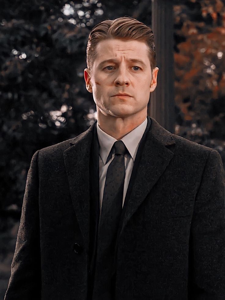 a man wearing a suit and tie standing in front of trees