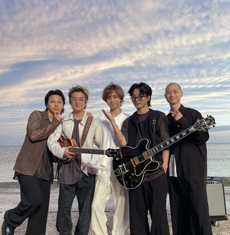 four people posing for a photo with an electric guitar in front of the ocean and sky