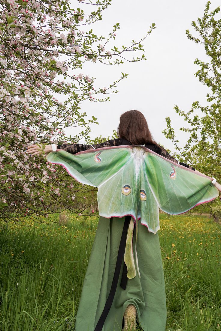 a woman in a green kimono with a large butterfly on her back, walking through the grass