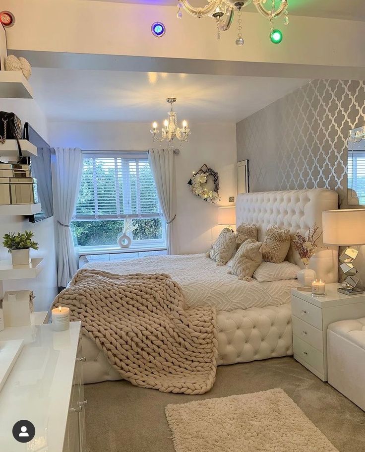 a bedroom with white furniture and chandelier above the bed is decorated in neutral colors