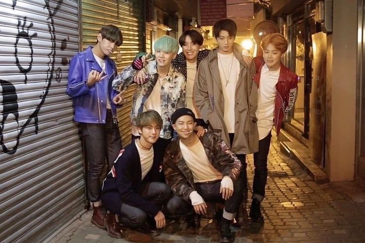 a group of young men standing next to each other in front of a graffiti covered wall