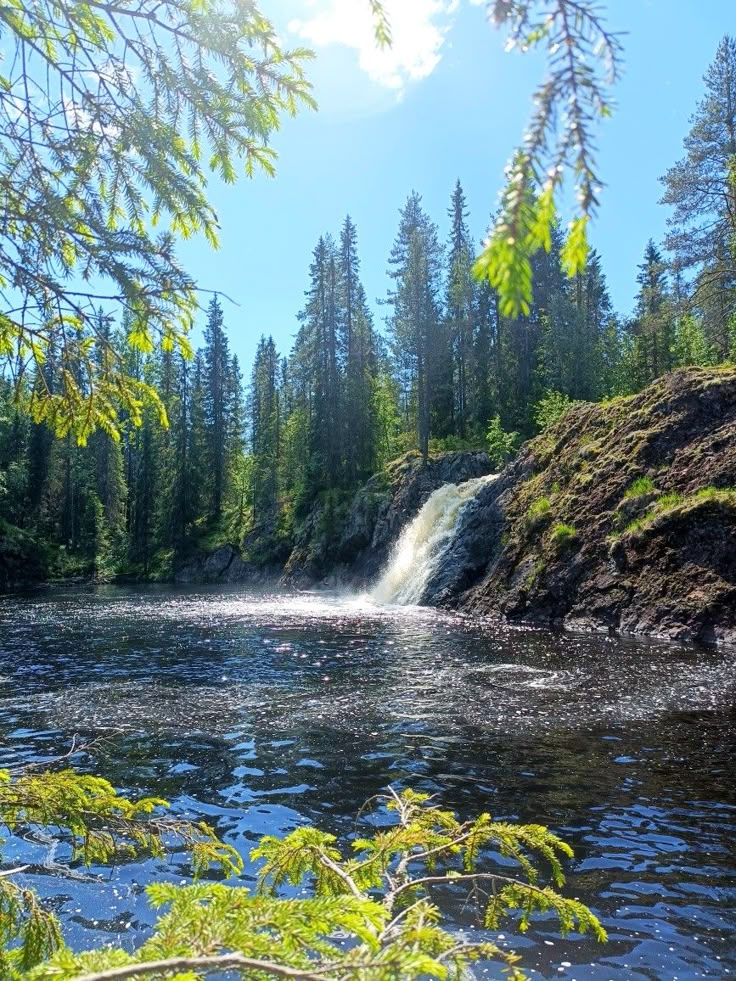 a small waterfall in the middle of a lake surrounded by trees and rocks with water running down it