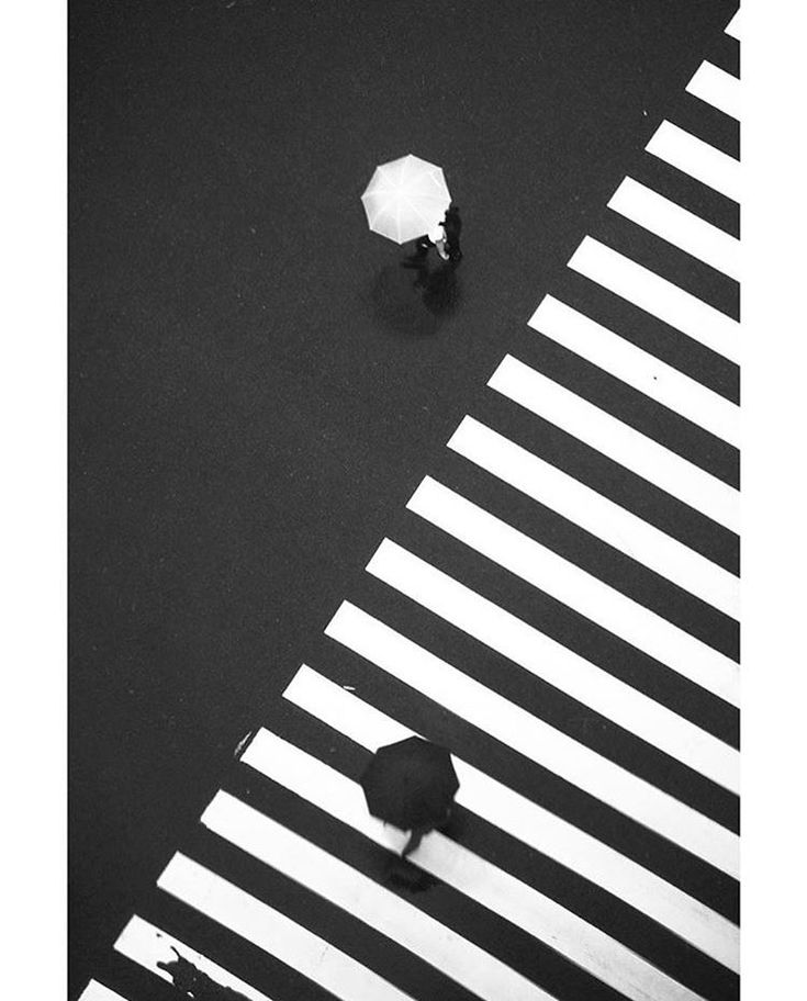 two people with umbrellas walking across a crosswalk in black and white, from above