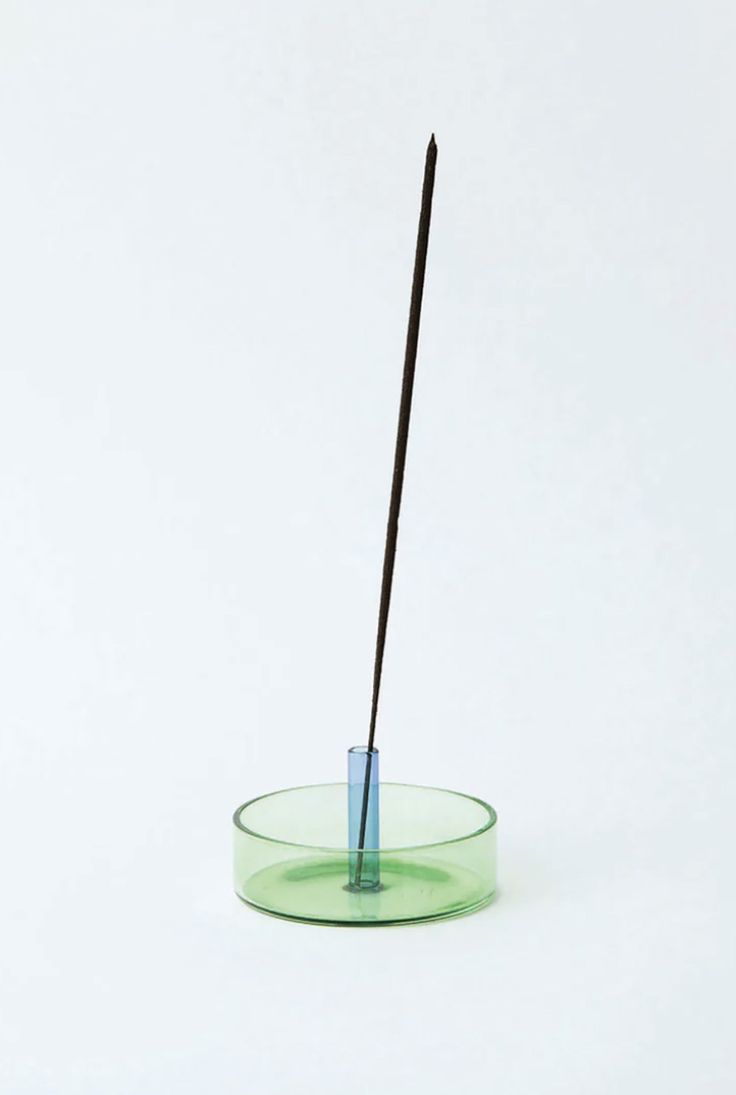 a green glass bowl with a black stick sticking out of the top, on a white background