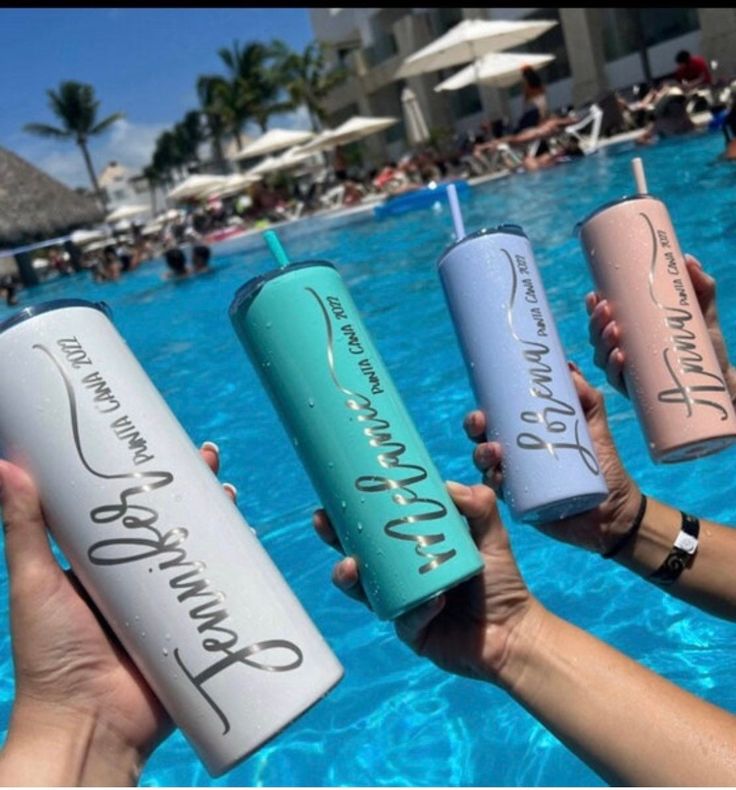 four people holding up water bottles in front of a swimming pool with the words drink on them