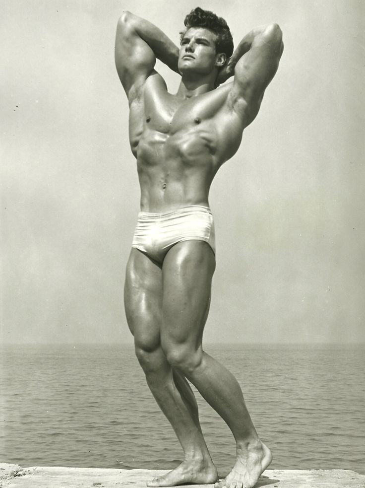 a man standing on top of a wooden pier next to the ocean with his hands behind his head