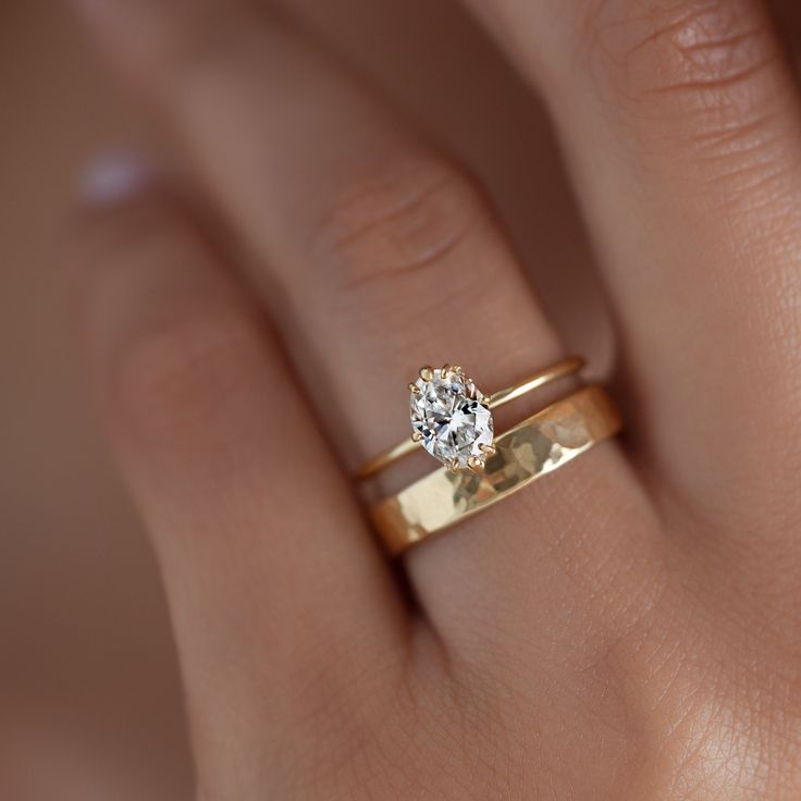 a woman's hand with a gold ring and diamond engagement ring on her finger