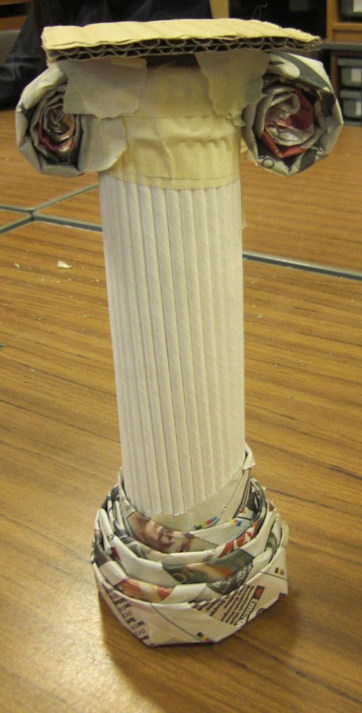 a white vase sitting on top of a wooden floor next to a cup with newspaper wrapped around it