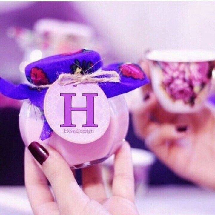 a woman holding two cups with the letter h on them and one has a purple ribbon around it