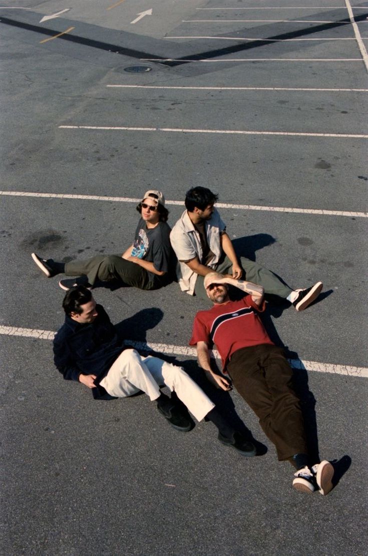 four men laying on the ground in an empty parking lot