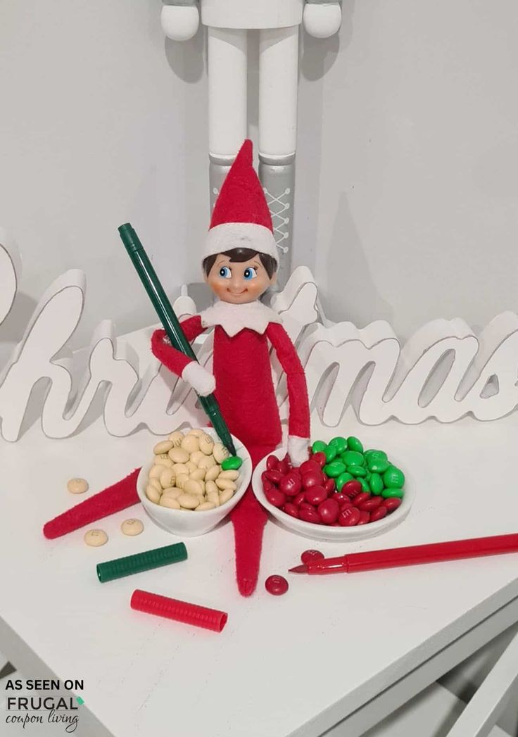 an elf is sitting on top of a table with some candy and nuts in front of him