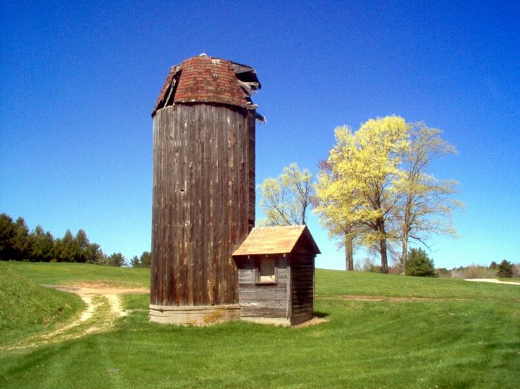 an old wooden silo sitting in the middle of a field next to a tree