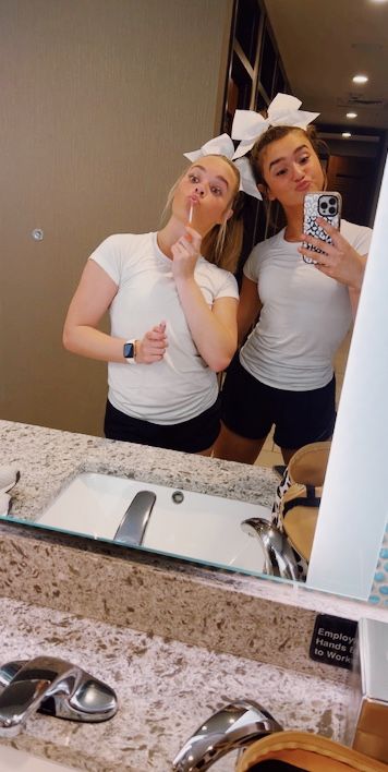 two women taking a selfie in front of a bathroom mirror