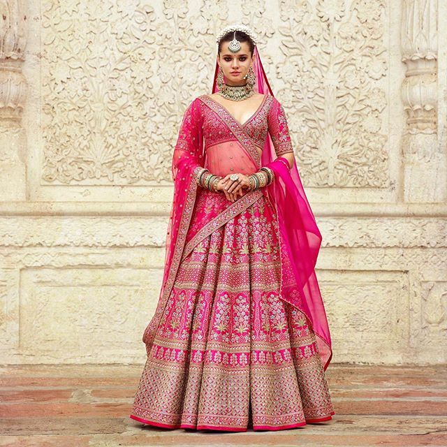 a woman in a pink and gold bridal gown standing next to a white wall