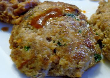 three meat patties on a white plate with sauce drizzled over them