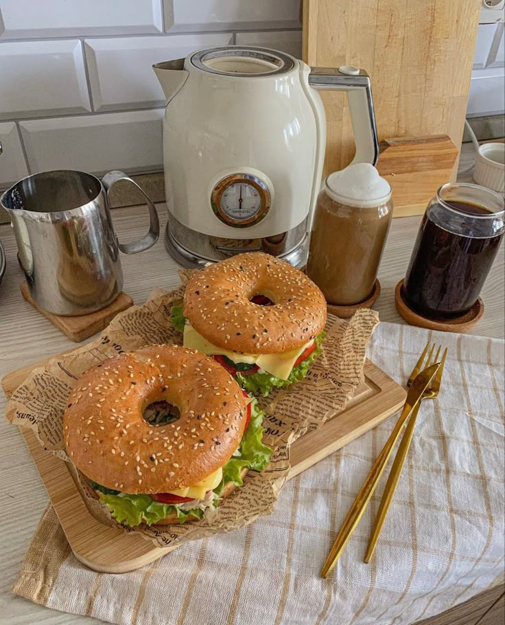 two hamburgers sitting on top of a cutting board next to a cup of coffee