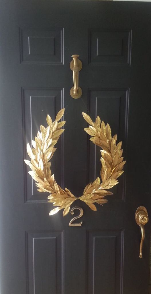 a black door with a gold wreath on it and the number two in front of it