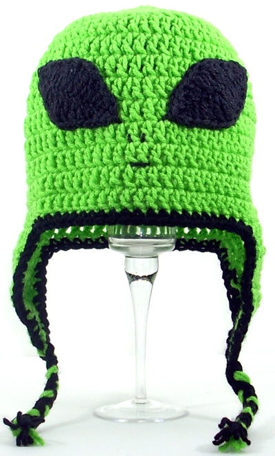 a crocheted green hat with black eyes on top of a wine goblet