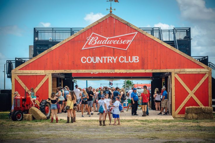 a group of people standing in front of a red barn with the words budweiser country club on it