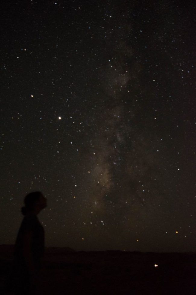 a person standing on top of a sandy beach under a night sky filled with stars