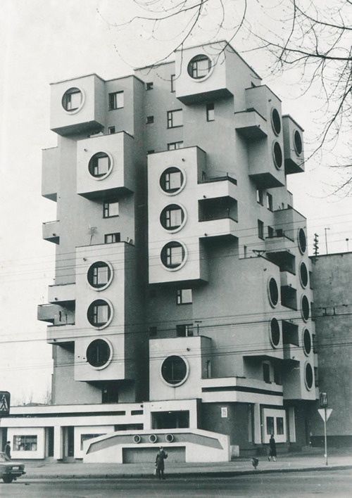 a tall building with lots of windows and round holes on the front is shown in black and white