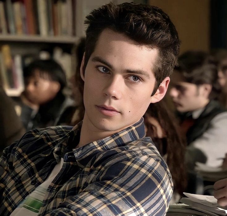 a young man sitting in front of a book shelf