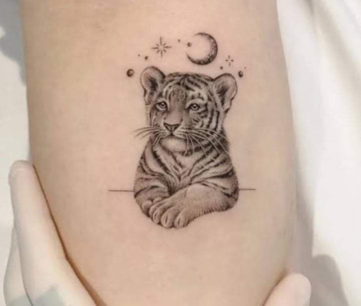 a small tiger cub tattoo on the left thigh and right leg with crescent moon behind it