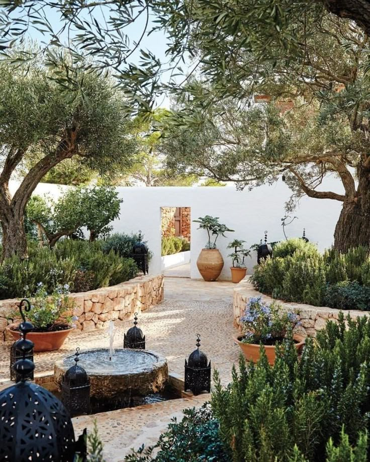 an outdoor courtyard with potted plants and trees in the foreground, surrounded by stone walls