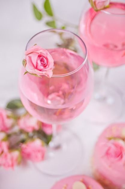 two wine glasses filled with pink liquid and roses on the table next to each other