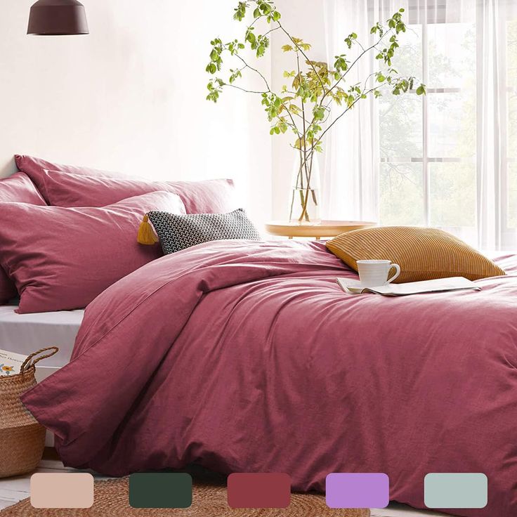 a bed with pink sheets and pillows in front of a potted plant next to a window