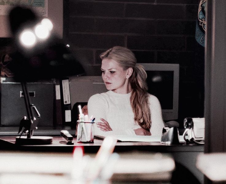 a woman sitting at a desk in front of a computer monitor with her arms crossed