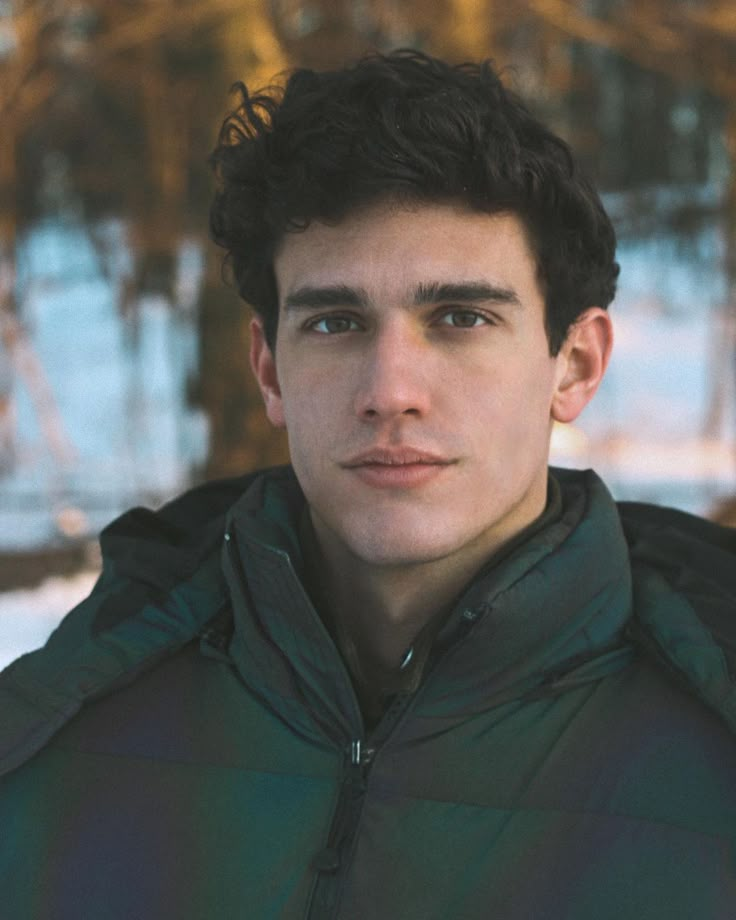 a young man is standing in the snow wearing a green jacket and looking at the camera