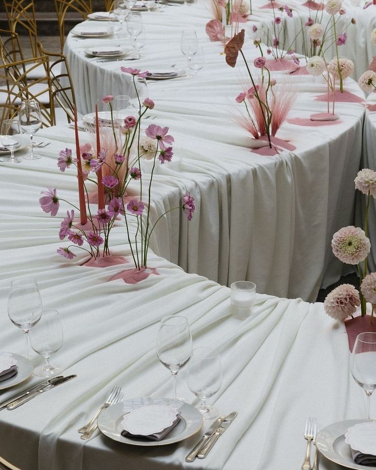 the tables are set with white linens and pink flowers in vases on them