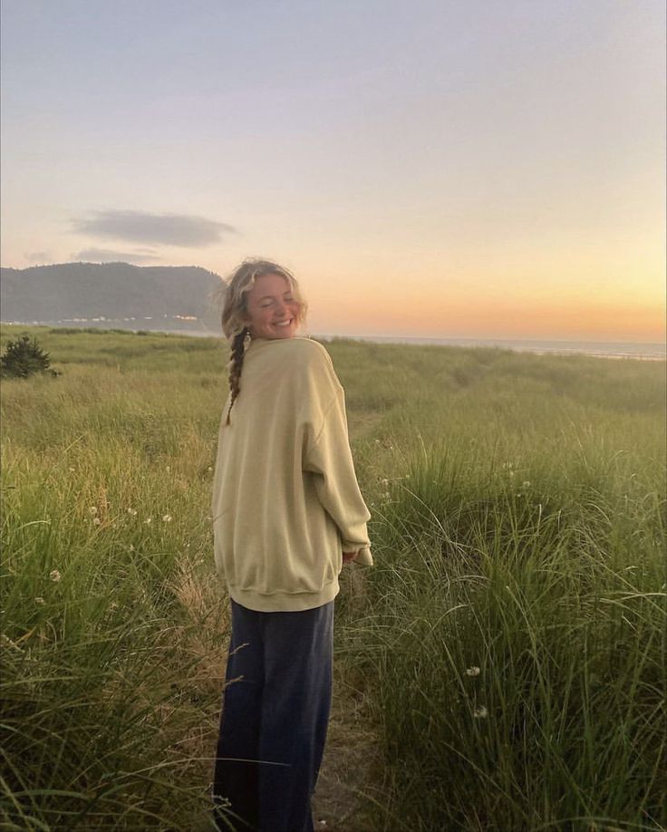 a woman standing in tall grass near the ocean