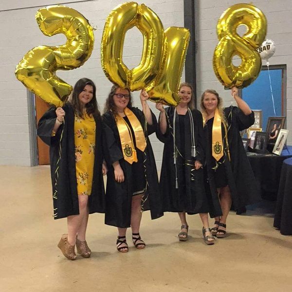 three girls in graduation gowns holding up gold balloons that spell out the number 80