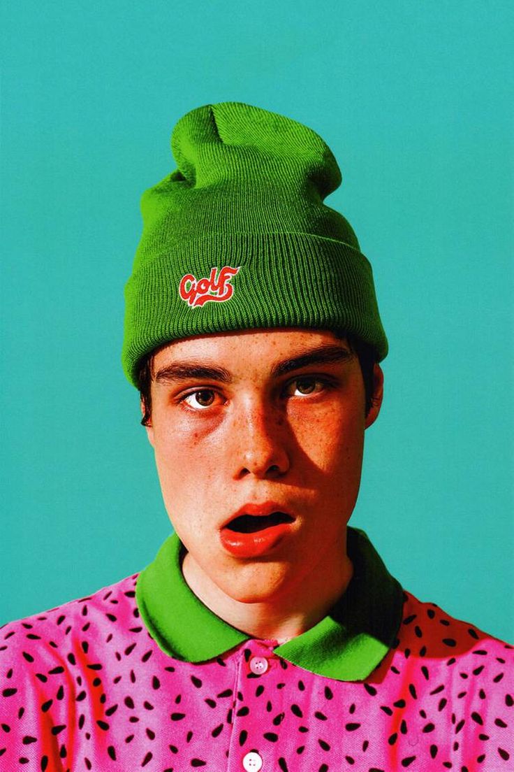 a young man wearing a green beanie and pink shirt with polka dots on it